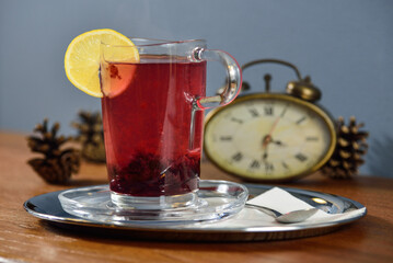 Glass cup of tea with lemon on a wooden table with an alarm clock in the background