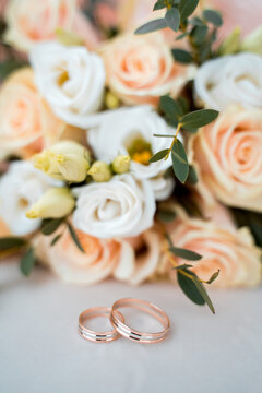 wedding rings lie on a white table next to a bouquet of beautiful fresh roses