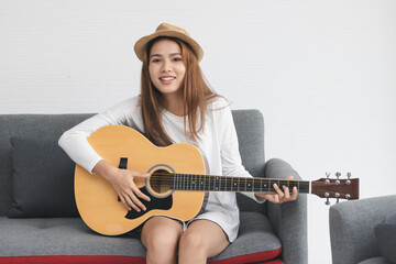 Happy cheerful Asian woman playing acoustic guitar in living room. Music lover concept.