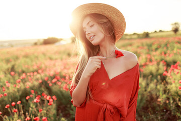 Romantic  blonde woman with flower in hand walking in amazing poppy field. Warm   sunset colors.