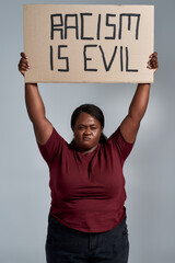 Fierce plus size young african american woman in casual clothes looking at camera, holding Racism...