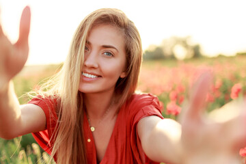 Fresh lovely blond woman making self portrait while walking along the poppy field .