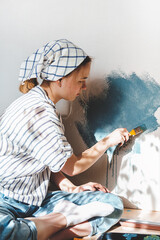 young girl paints the wall of the house with a roller in blue. Gender equality, stereotypes, March...