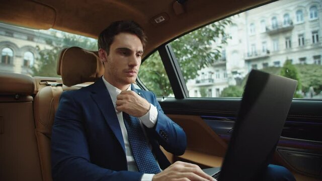 Portrait of focused business man typing on laptop computer in modern car.