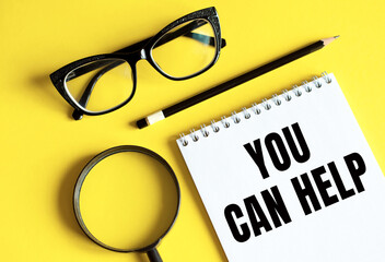 New YOU CAN HELP text written on a notebook with glasses, magnifying glass and pencil.