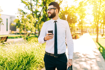 businessman with glasses uses mobile phone while walking in the city