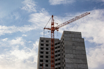 A crane near a house under construction against the blue sky.