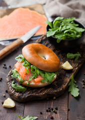 Fresh healthy organic sandwich with bagel and salmon, cream cheese and wild rocket on chopping board with smoked salmon pack.