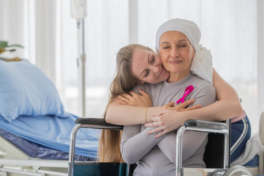 A middle-aged breast cancer woman with clothing around her head effected from chemo therapy sitting on wheel chair and hold hand of her daughter with hope and trust in love.
