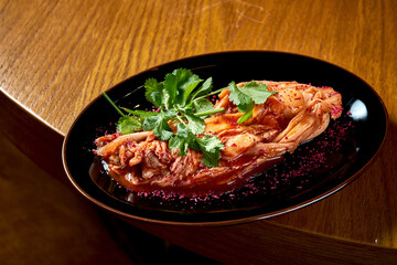 A traditional Korean dish is spicy Chinese cabbage kimchi with spices and hot sauce, served in a black plate on a wooden background. View from above