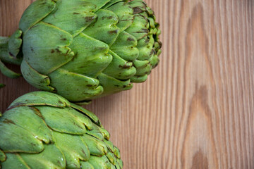 Fototapeta premium Aerial view of two green artichokes, on rustic wooden table, horizontally, with copy space
