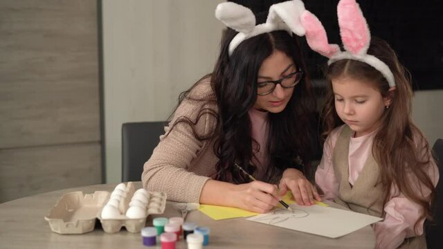 Cheerful family is preparing for the Easter holiday mom and daughter draw a hare on paper.