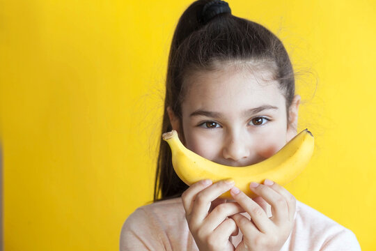 Happy little child girl with yellow banana like smile on yellow background.