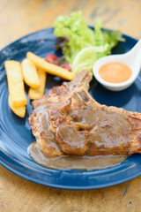 Pork chop french fries sot on a blue plate on a wooden table