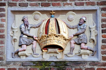 Old stone tablet of two men holding a golden crown, a carved and colorfully painted stone tablet on a brick wall in the old center of Amsterdam, serving both to identify and embellish the building