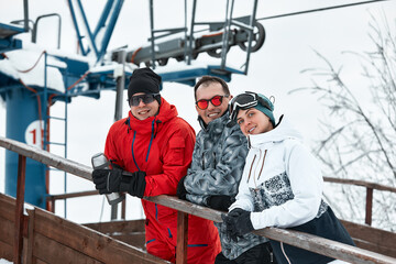 group of skiers friends on the mountain are resting and drinking coffee from a thermos on the background of the ski lift