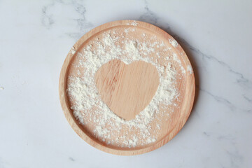 Heart of the flour on wooden plate   on marble background. prepation for cooking homemade cookise. top view, love concept. 