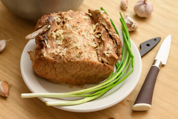 cauldron of soup and baked meat on a plate, green onion and garlic on wooden background, home cooking