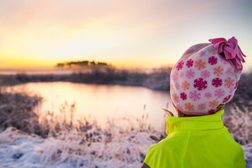 Little kid at frozen lake in winter landscape