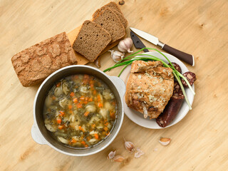 baked meat, soup and blood sausage on a plate, green onion and garlic on wooden background, home...