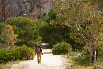 Climber with full rucksack going toward a scenic limestone crag in San Vito lo Capo in Sicily