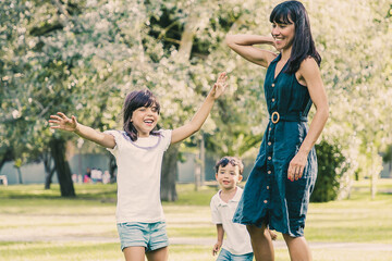 Two joyful kids and their mom playing active games on grass, having fun together in park. Family outdoor activity and leisure concept