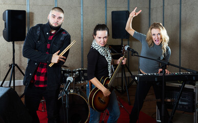 Fototapeta na wymiar Expressive active group of rock musicians posing with instruments in recording studio