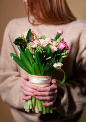 Attractive stylish ginger hair girl in beige sweater holds flower bouquet in spring theme. Mother's Day, St. Valentine's day or International Woman's Day concept