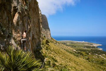 young caucasian man climbing on a limestone crag near San Vito lo Capo in Sicily with wide panoramic view 2
