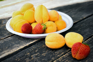 Fresh apricots and strawberry on the wooden table background close up.