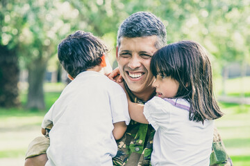 Happy military father meeting with children after military mission trip, holding kids in arms and smiling. Family reunion or returning home concept