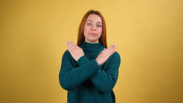 Young woman crossing hands in stop gesture, definitely rejecting suggestion, warning of trouble, declining with negative expression. Shot isolated on yellow background