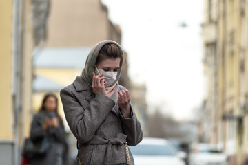 Fototapeta premium Young pretty woman in coat outdoors in medical mask talking on the phone, copy space
