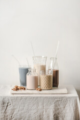 Dairy-free milk assortment with different flavours. Almond milk with blue matcha, berries, coffee, cinnamon, cocoa in bottles and glasses on counter, white background, copy space. Vegan, healthy food
