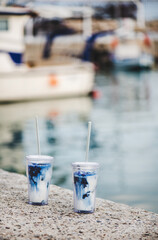 Blue iced matcha latte drink in reusable eco-friendly glasses with glass straws at sea coast in Mediterranean town, selective focus. Take away food during lockdown concept