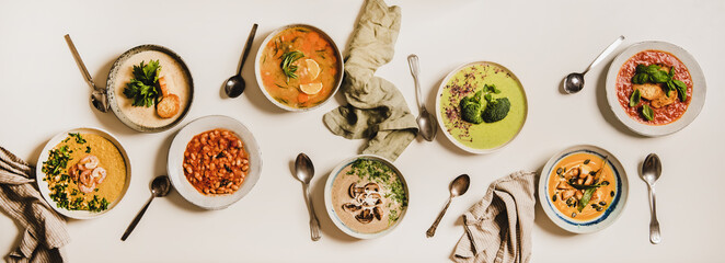 Flat-lay of vegetarian creamy homemade soup and spoons over white plain table background, top view....