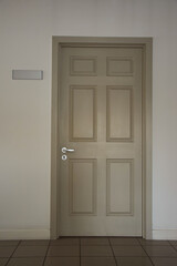 Closed light door of an office space with a blank sign on the left side on the wall