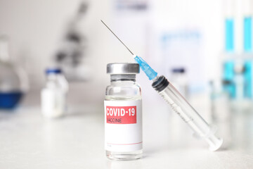 Vial with vaccine against Covid-19 and syringe on white table indoors