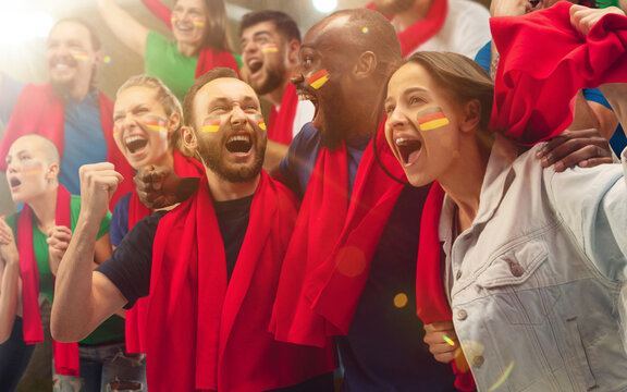 German football, soccer fans cheering their team with a red scarfs at stadium. Excited fans cheering a goal, supporting favourite players. Concept of sport, human emotions, entertainment.