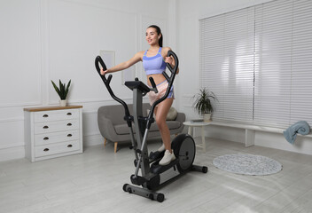 Fototapeta na wymiar Happy young woman training on elliptical machine at home