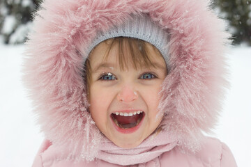 Portrait of a laughing little girl in winter clothes in the snow in winter close-up, childrens emotions happy childhood, selective focus	