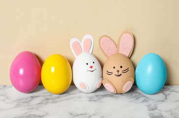 Two eggs as cute bunnies among others on white marble table against beige background. Easter celebration