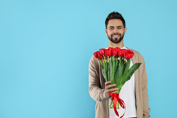 Obraz premium Happy man with red tulip bouquet on light blue background, space for text. 8th of March celebration