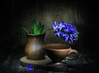 Still life with blue flowers in a vase and a cup of coffee on a wooden board.