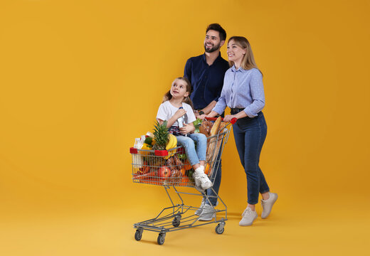 Happy family with shopping cart full of groceries on yellow background