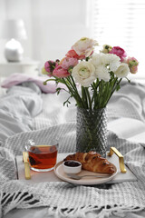 Bouquet of beautiful ranunculuses, croissant and tea on bed indoors