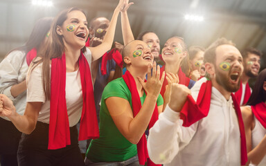 Brazilian football, soccer fans cheering their team with a red scarfs at stadium. Excited fans cheering a goal, supporting favourite players. Concept of sport, human emotions, entertainment.