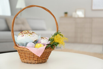 Fototapeta na wymiar Basket with delicious Easter cakes, dyed eggs and flowers on white table indoors. Space for text