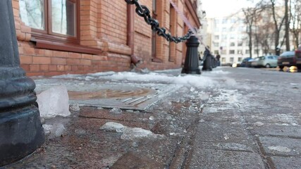 Wet snow with ice and icicles lies on the sidewalk that has fallen from the rear roof. Concept of risk of injury from ice falling from the roof in the city