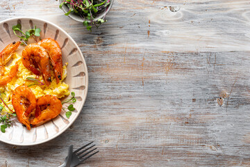 Scrambled eggs with cheese and shrimps on a wooden background, copy space.